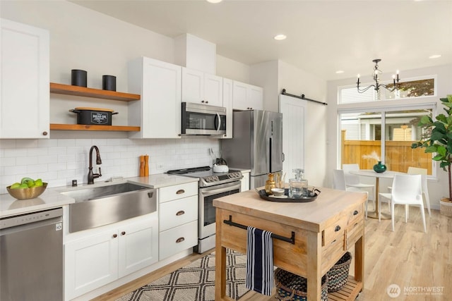 kitchen featuring appliances with stainless steel finishes, a sink, light countertops, a barn door, and decorative backsplash