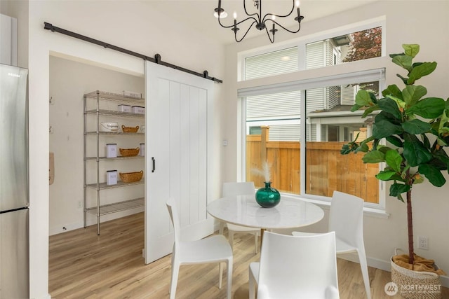 dining room with a barn door, wood finished floors, a chandelier, and baseboards