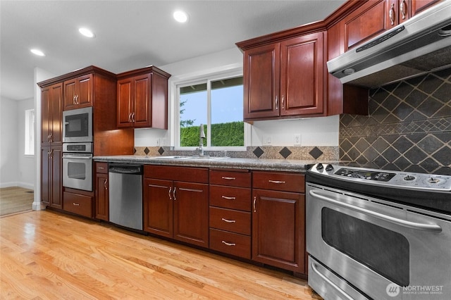 16912 49th St E, Lake Tapps, WA 98391 - kitchen featuring appliances with stainless steel finishes, under cabinet range hood, light wood-style floors, dark countertops, and a sink