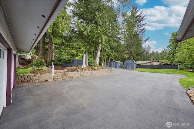 view of patio with a storage unit, an outbuilding, driveway, fence, and view of wooded area