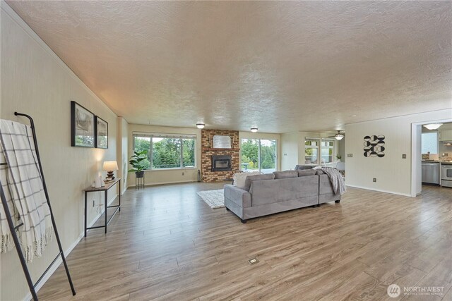 living room with a textured ceiling, light wood-type flooring, baseboards, a fireplace, and ceiling fan