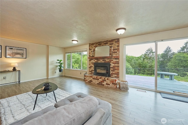 living room with wood finished floors, a textured ceiling, a brick fireplace, and baseboards