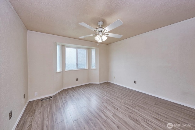 unfurnished room featuring wood finished floors, a ceiling fan, baseboards, a textured wall, and a textured ceiling