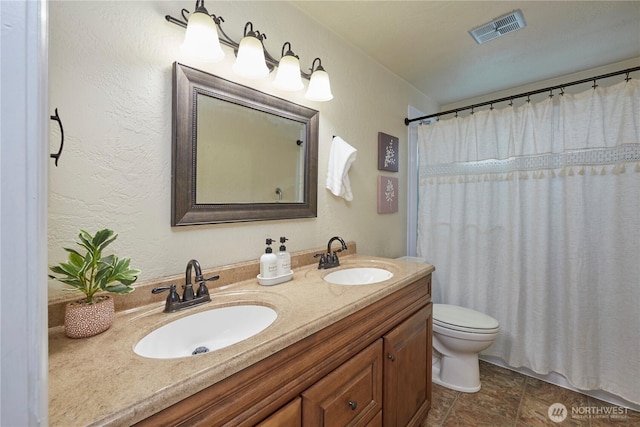 bathroom with toilet, double vanity, and a textured wall