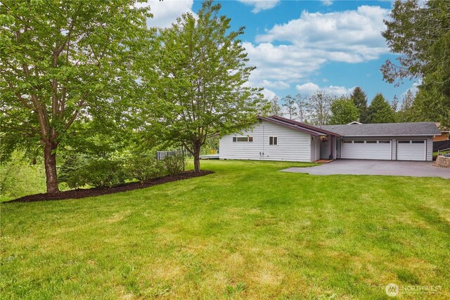 view of green lawn with a garage and asphalt driveway