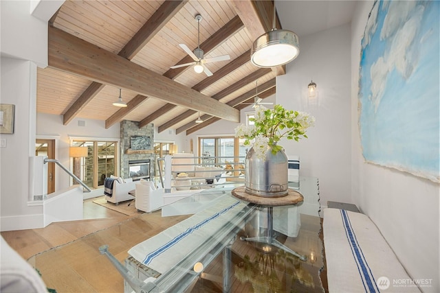 dining space featuring beam ceiling, wooden ceiling, a stone fireplace, a ceiling fan, and high vaulted ceiling