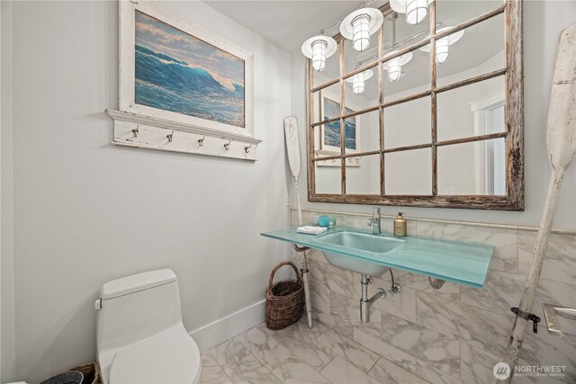 half bathroom featuring marble look tile flooring, toilet, a sink, and baseboards