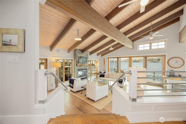 living room featuring ceiling fan, wooden ceiling, a fireplace, light wood-style floors, and beamed ceiling