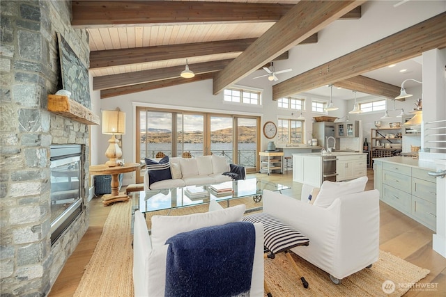 living area with a ceiling fan, a stone fireplace, a water view, wooden ceiling, and light wood-style floors