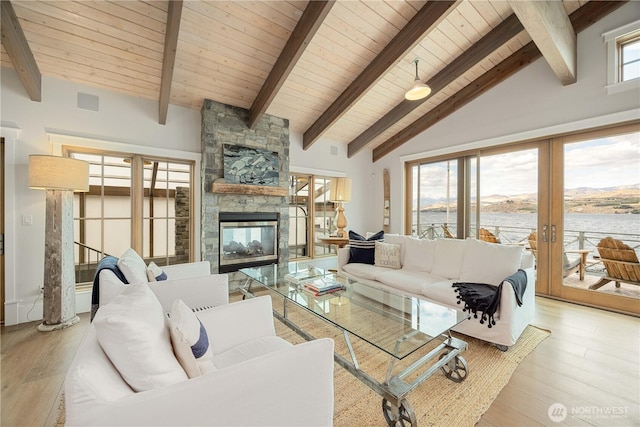 living room featuring beam ceiling, a fireplace, light wood-type flooring, wooden ceiling, and a water view