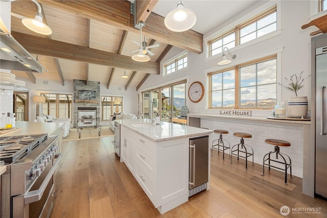 kitchen with wine cooler, beam ceiling, light wood-type flooring, stainless steel range, and white cabinets