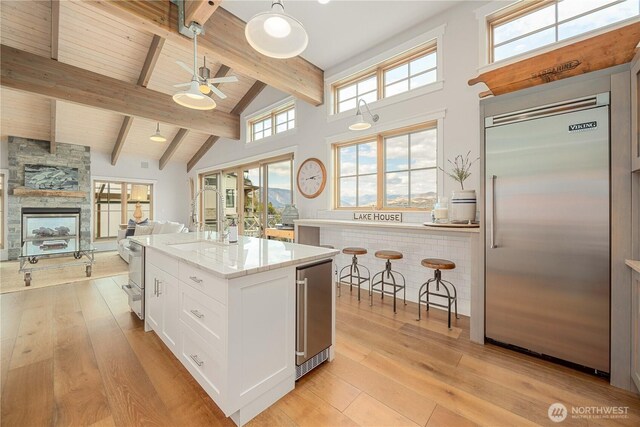 kitchen featuring stainless steel built in refrigerator, a ceiling fan, beam ceiling, light stone countertops, and light wood-style floors