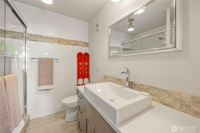 full bathroom with a shower stall, tile walls, vanity, and toilet