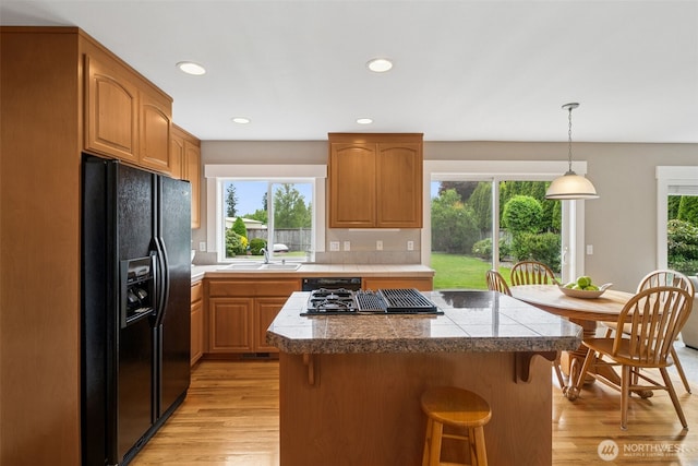 1855 Shanon Ln, Enumclaw, WA 98022 - kitchen featuring black appliances, a center island, tile counters, light wood-style flooring, and a breakfast bar area