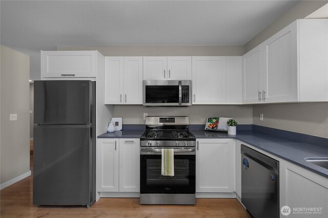 kitchen with appliances with stainless steel finishes, dark countertops, white cabinetry, and light wood-type flooring