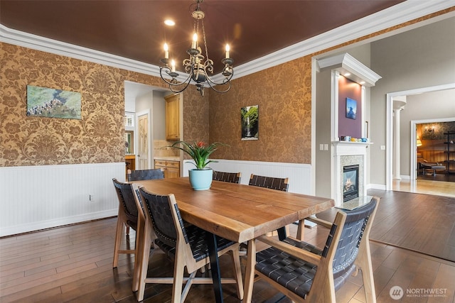 dining area with wainscoting, a chandelier, hardwood / wood-style floors, ornamental molding, and a glass covered fireplace