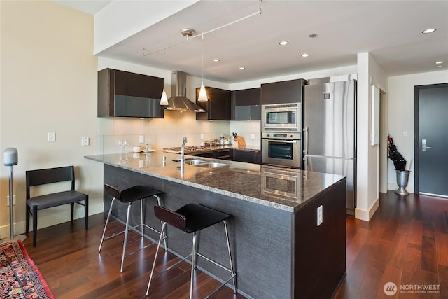 737 Olive Way Unit 2703, Seattle, WA 98101 - kitchen with wall chimney range hood, stainless steel appliances, dark stone countertops, a peninsula, and dark wood-type flooring