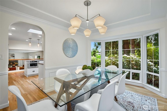 dining room featuring arched walkways, light wood finished floors, crown molding, and wainscoting