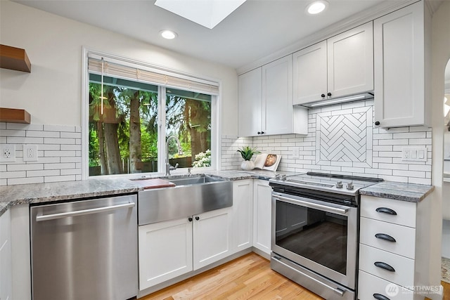 kitchen featuring stainless steel appliances, a skylight, a sink, open shelves, and decorative backsplash