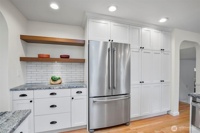 kitchen with high end refrigerator, arched walkways, open shelves, light wood finished floors, and white cabinets