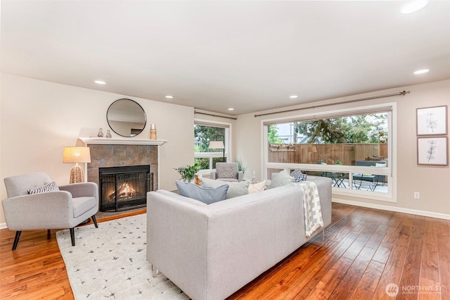 living room featuring light wood-type flooring, a tiled fireplace, baseboards, and recessed lighting
