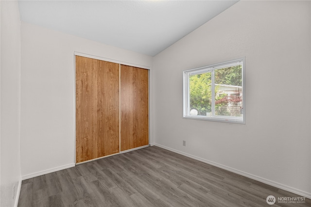 unfurnished bedroom featuring lofted ceiling, wood finished floors, a closet, and baseboards