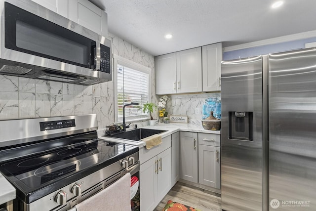 kitchen featuring appliances with stainless steel finishes, a sink, decorative backsplash, recessed lighting, and gray cabinetry