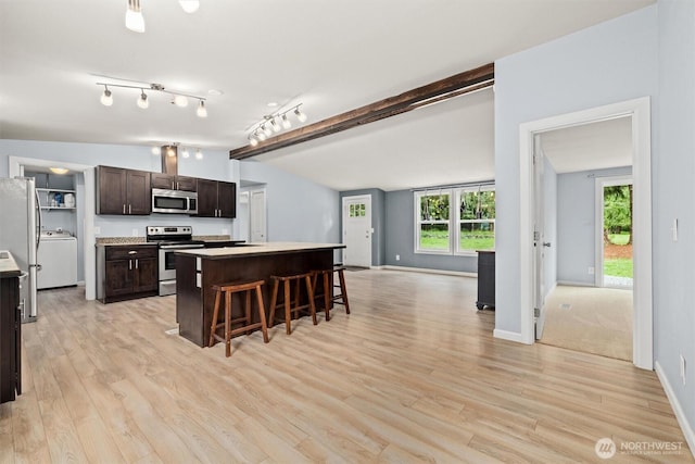 kitchen featuring appliances with stainless steel finishes, dark brown cabinetry, a kitchen breakfast bar, washer / clothes dryer, and light wood-style flooring