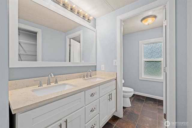 full bathroom with toilet, double vanity, baseboards, and stone finish floors