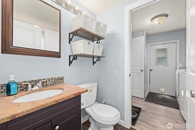 bathroom featuring washer and clothes dryer, wood finished floors, decorative backsplash, toilet, and vanity