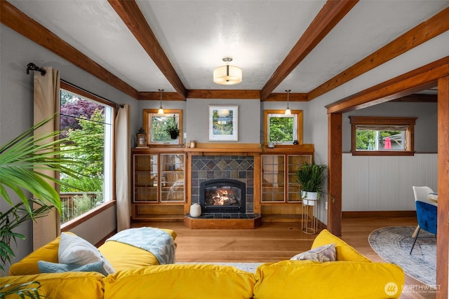 living area with wood finished floors, beamed ceiling, healthy amount of natural light, a fireplace, and baseboards