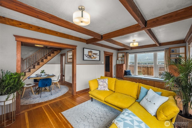 living room with stairs, hardwood / wood-style floors, beamed ceiling, wainscoting, and baseboards