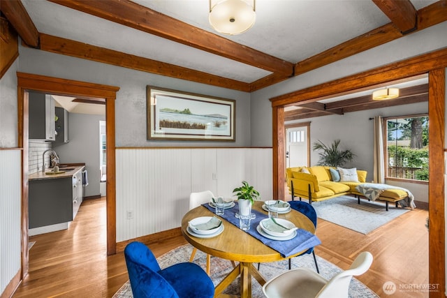 dining room with beamed ceiling, wainscoting, and light wood-style floors
