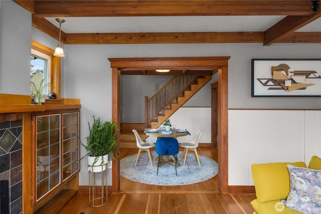 dining space featuring beamed ceiling, wood finished floors, stairs, and a wainscoted wall