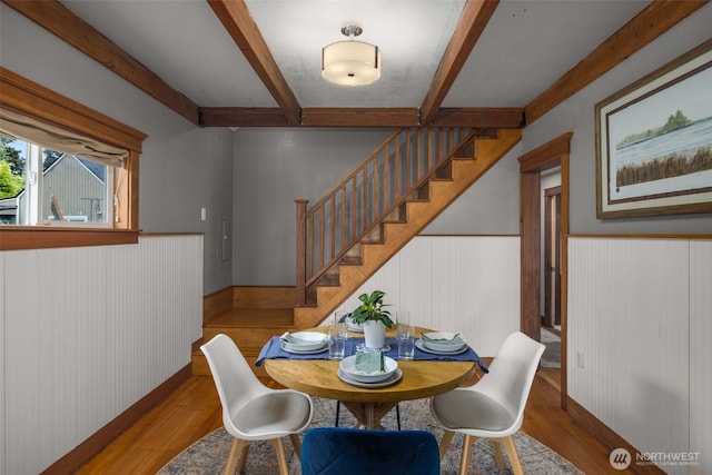 dining space with beam ceiling, stairway, wainscoting, wood finished floors, and wooden walls