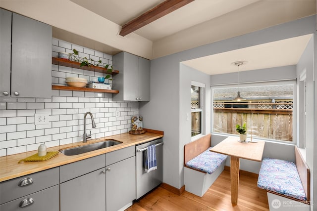 kitchen with gray cabinets, stainless steel dishwasher, a sink, light wood-type flooring, and beamed ceiling