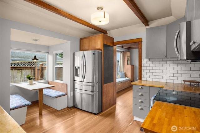 kitchen with appliances with stainless steel finishes, wooden counters, decorative backsplash, beamed ceiling, and light wood-style floors