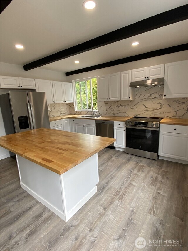 kitchen with wood counters, stainless steel appliances, under cabinet range hood, white cabinets, and beam ceiling
