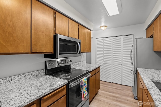 8516 196th St SW Unit 311, Edmonds, WA 98026 - kitchen featuring stainless steel appliances, light wood-type flooring, brown cabinetry, and light stone countertops