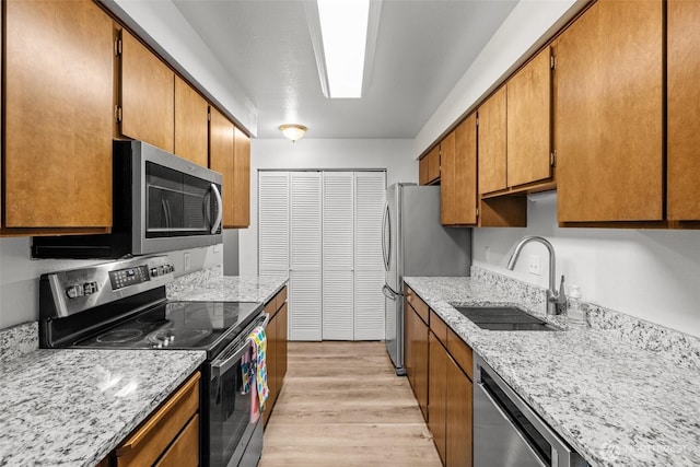 8516 196th St SW Unit 311, Edmonds, WA 98026 - kitchen with appliances with stainless steel finishes, a sink, light wood-type flooring, brown cabinets, and light stone countertops