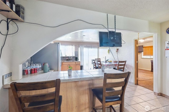 237 Reeds Rd, Touchet, WA 99360 - kitchen featuring tile counters, arched walkways, a breakfast bar area, freestanding refrigerator, and a textured ceiling