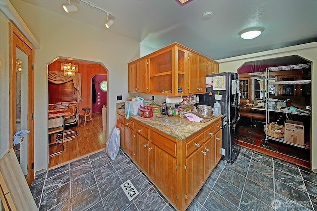 19308 8th St E, Spanaway, WA 09387 - kitchen featuring arched walkways, freestanding refrigerator, brown cabinetry, light stone countertops, and lofted ceiling