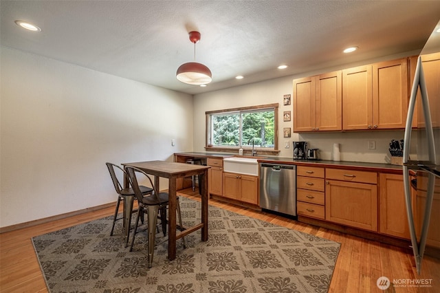 kitchen with stainless steel appliances, a sink, dark countertops, light wood finished floors, and recessed lighting