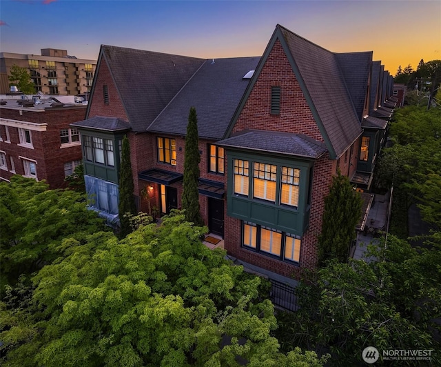back of property at dusk with brick siding and a shingled roof