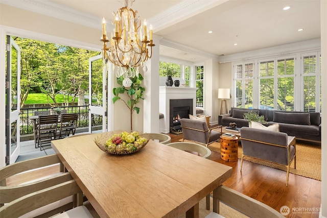 dining room with ornamental molding, a warm lit fireplace, a chandelier, wood finished floors, and recessed lighting