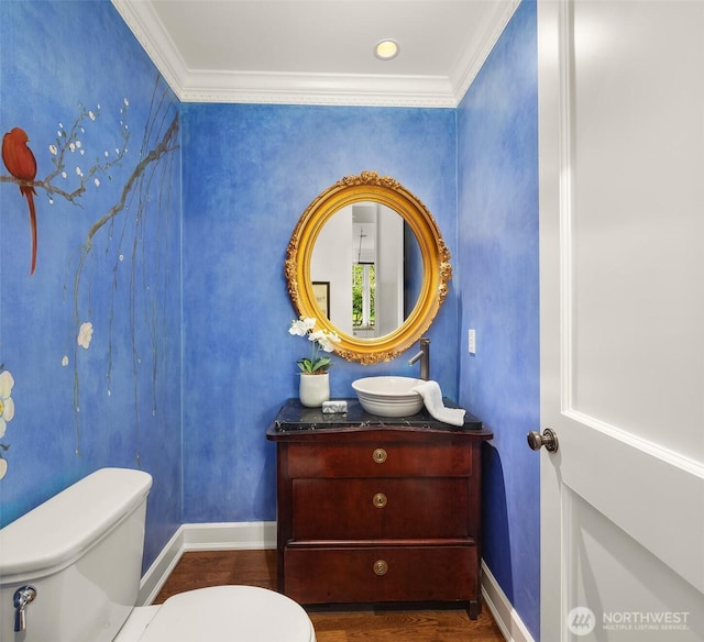 half bath with toilet, crown molding, wood finished floors, vanity, and baseboards