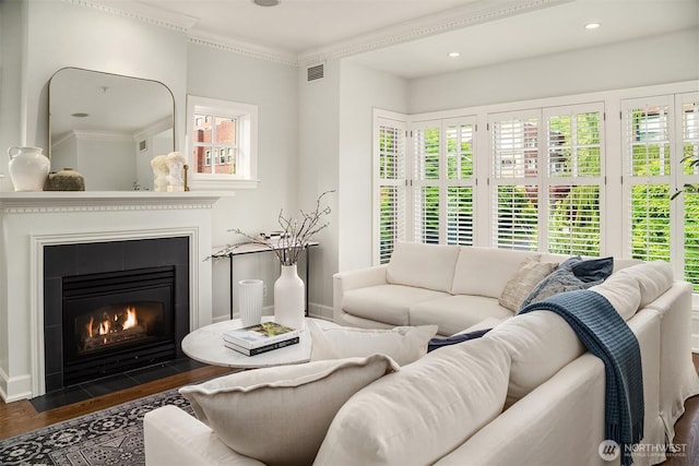 living room with wood finished floors, plenty of natural light, a fireplace with flush hearth, ornamental molding, and baseboards