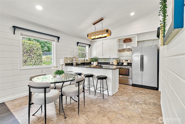 kitchen featuring appliances with stainless steel finishes, open shelves, dark countertops, a sink, and a peninsula