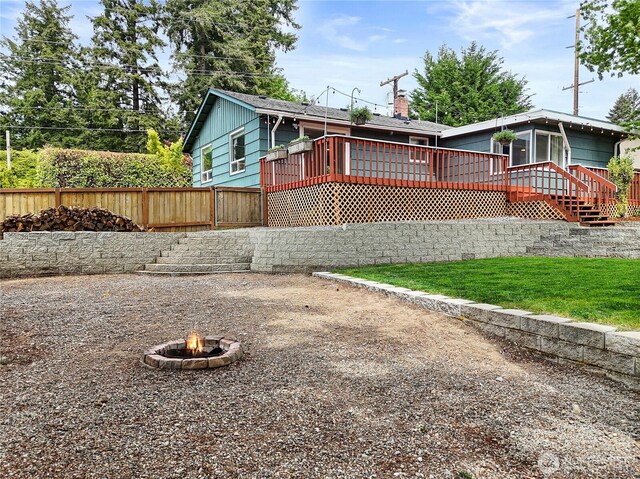 view of front of house featuring an outdoor fire pit, a wooden deck, fence, a chimney, and a sunroom