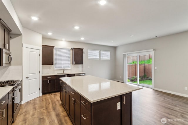 kitchen with appliances with stainless steel finishes, a kitchen island, decorative backsplash, light wood finished floors, and recessed lighting
